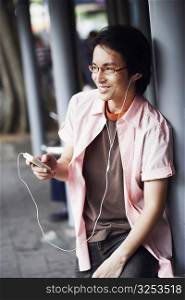 Close-up of a mid adult man leaning against a pole and listening to an MP3 player