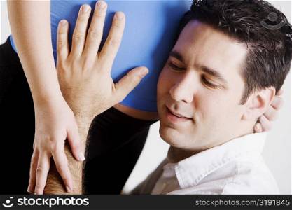 Close-up of a mid adult man listening to a pregnant young woman&acute;s abdomen