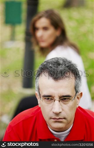 Close-up of a mid adult man looking sad with a mid adult woman sitting behind him