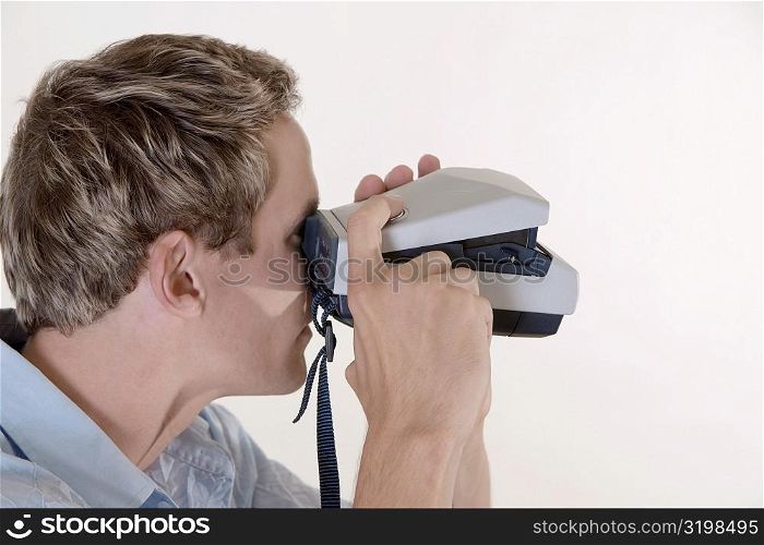 Close-up of a mid adult man looking through an instant camera