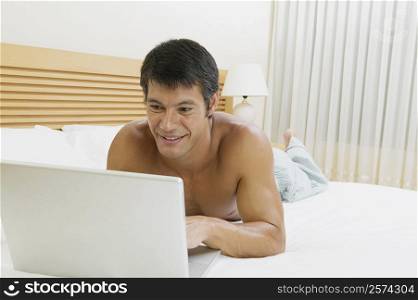 Close-up of a mid adult man lying on the bed using a laptop