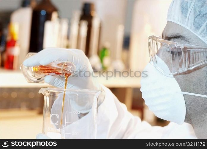 Close-up of a mid adult man pouring liquid from a measuring beaker into a beaker