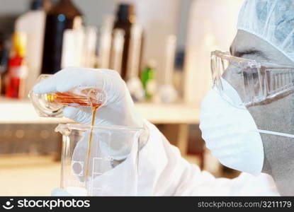 Close-up of a mid adult man pouring liquid from a measuring beaker into a beaker