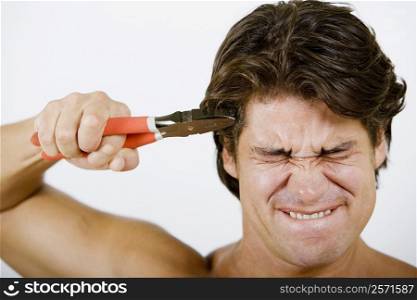 Close-up of a mid adult man pressing pliers up to his head