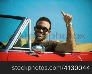 Close-up of a mid adult man sitting in a convertible car pointing forward, Miami, Florida, USA