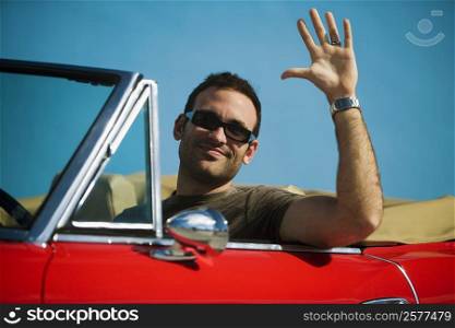 Close-up of a mid adult man sitting in a convertible car waving his hand, Miami, Florida, USA