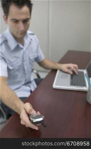 Close-up of a mid adult man sitting in front of a laptop and using a mobile phone