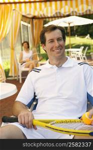 Close-up of a mid adult man sitting on a chair holding a tennis ball and a tennis racket