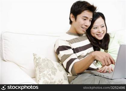 Close-up of a mid adult man sitting on a couch with a young woman using a laptop