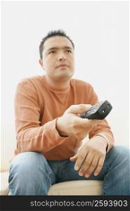 Close-up of a mid adult man sitting on couch and operating a remote control