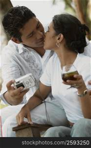 Close-up of a mid adult man taking a photograph of himself and kissing a mid adult woman