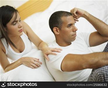 Close-up of a mid adult man thinking with a young woman lying on the bed