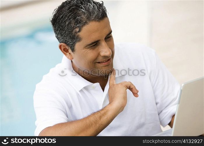 Close-up of a mid adult man using a laptop at the poolside