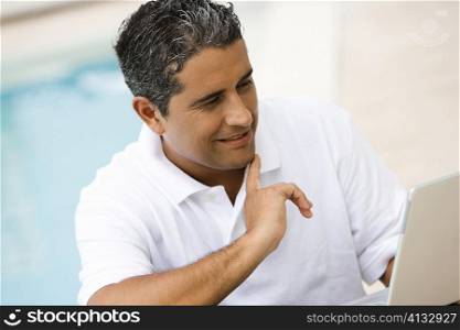 Close-up of a mid adult man using a laptop at the poolside