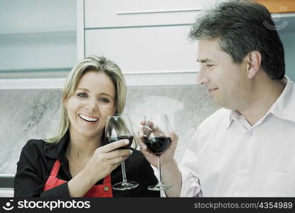 Close-up of a mid adult woman and a mature man toasting glasses of wine and smiling