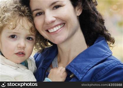 Close-up of a mid adult woman carrying her daughter and smiling