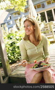 Close-up of a mid adult woman eating vegetable salad and smiling
