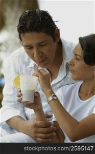 Close-up of a mid adult woman feeding a glass of juice to a mid adult man