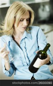 Close-up of a mid adult woman holding a bottle of wine and a wine glass