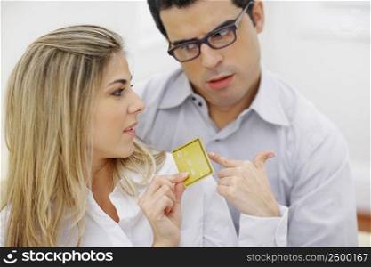 Close-up of a mid adult woman holding a credit card with a mid adult man looking at her