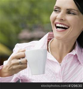 Close-up of a mid adult woman holding a cup of coffee and laughing