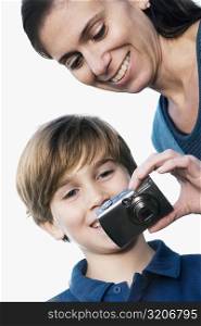 Close-up of a mid adult woman holding a digital camera and smiling with her son