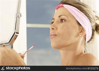 Close-up of a mid adult woman holding a mirror and a lip liner