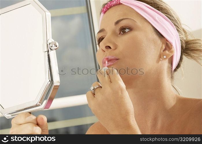 Close-up of a mid adult woman holding a mirror applying lipstick