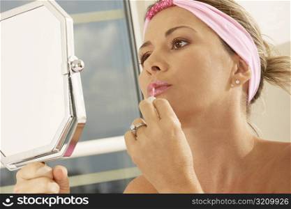 Close-up of a mid adult woman holding a mirror applying lipstick