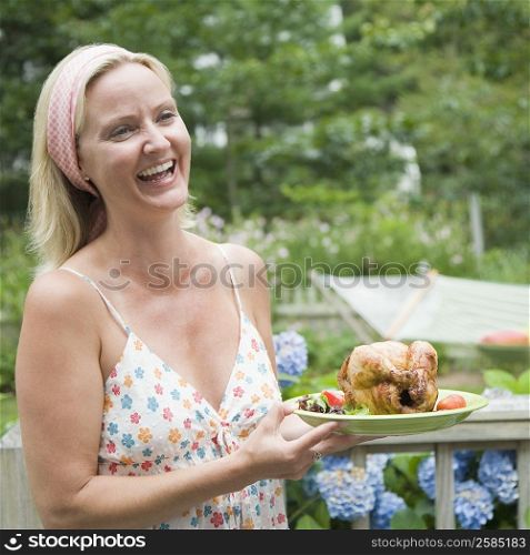 Close-up of a mid adult woman holding a plate of roast chicken and smiling