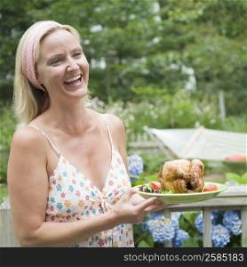 Close-up of a mid adult woman holding a plate of roast chicken and smiling