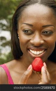 Close-up of a mid adult woman holding a strawberry and smiling