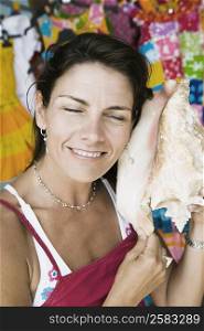 Close-up of a mid adult woman listening to a conch shell and smiling