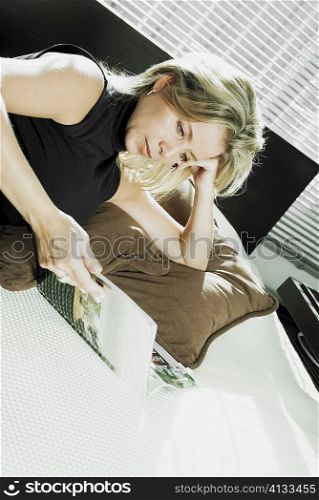 Close-up of a mid adult woman lying on the bed and reading a magazine
