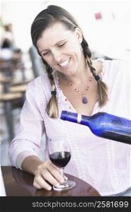 Close-up of a mid adult woman pouring wine into a wine glass and smiling