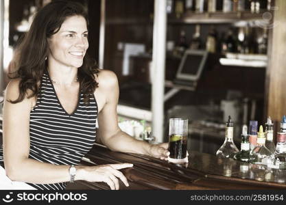 Close-up of a mid adult woman sitting at a bar counter and holding a glass of whiskey