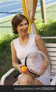 Close-up of a mid adult woman sitting on a chair and holding a tennis ball and a tennis racket