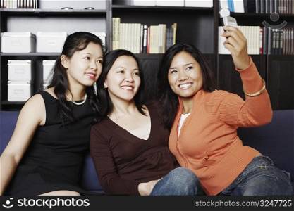 Close-up of a mid adult woman sitting with two young women on a couch taking a photograph of themselves