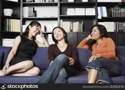 Close-up of a mid adult woman sitting with two young women on a couch smiling
