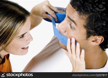 Close-up of a mid adult woman sticking an adhesive tape on a young man&acute;s mouth