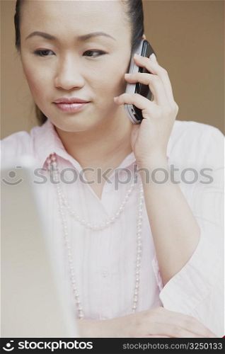 Close-up of a mid adult woman talking on a mobile phone and looking at a laptop