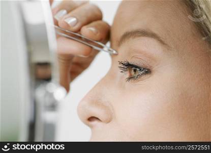 Close-up of a mid adult woman tweezing her eyebrows