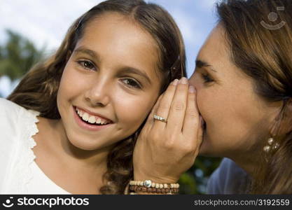 Close-up of a mid adult woman whispering into her daughter&acute;s ear