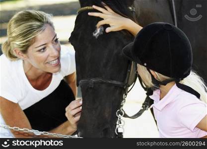 Close-up of a mid adult woman with her daughter touching a horse