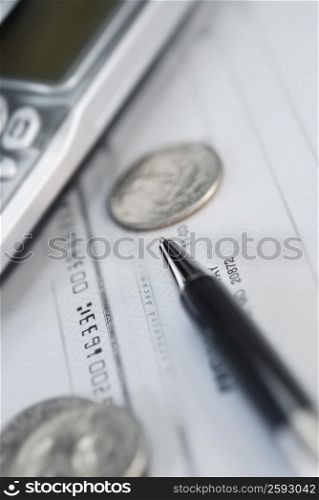 Close-up of a mobile phone and a pen with coins on a check