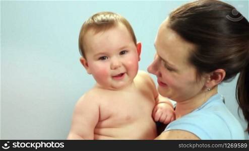 Close-up of a mother holding a happy baby boy against a light blue wall
