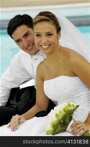 Close-up of a newlywed couple sitting at the poolside and smiling