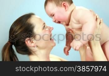 Close-up of a nude mother and baby playing against a light blue wall in slow-motion.