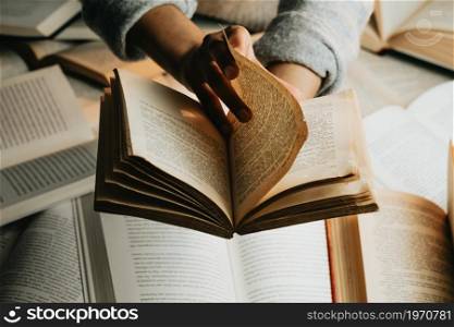 Close up of a pair of black hands reading an old book with copy space over a bunch of books