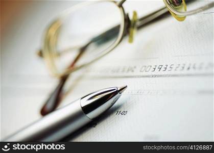Close-up of a pen and eyeglasses on a check